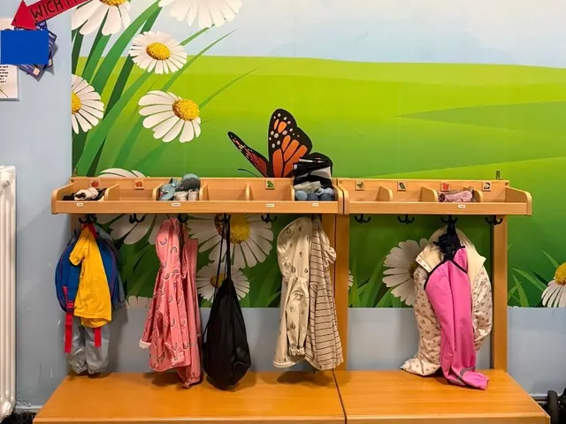 Garderobe mit Holzbank, Haken mit Jacken und einem Wandbild mit Regenbogen, Wiese und Schmetterlingen